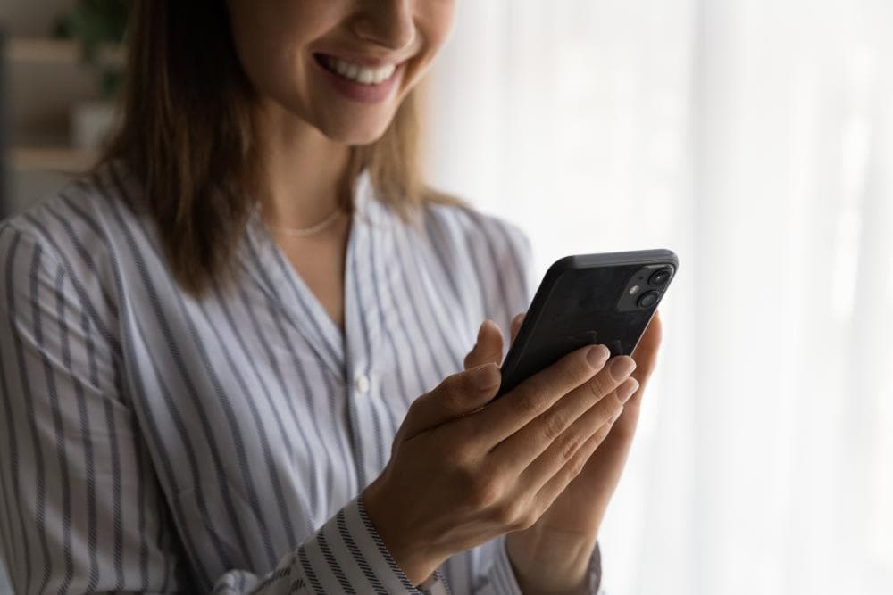 A woman smiling after receiving an SMS on her phone